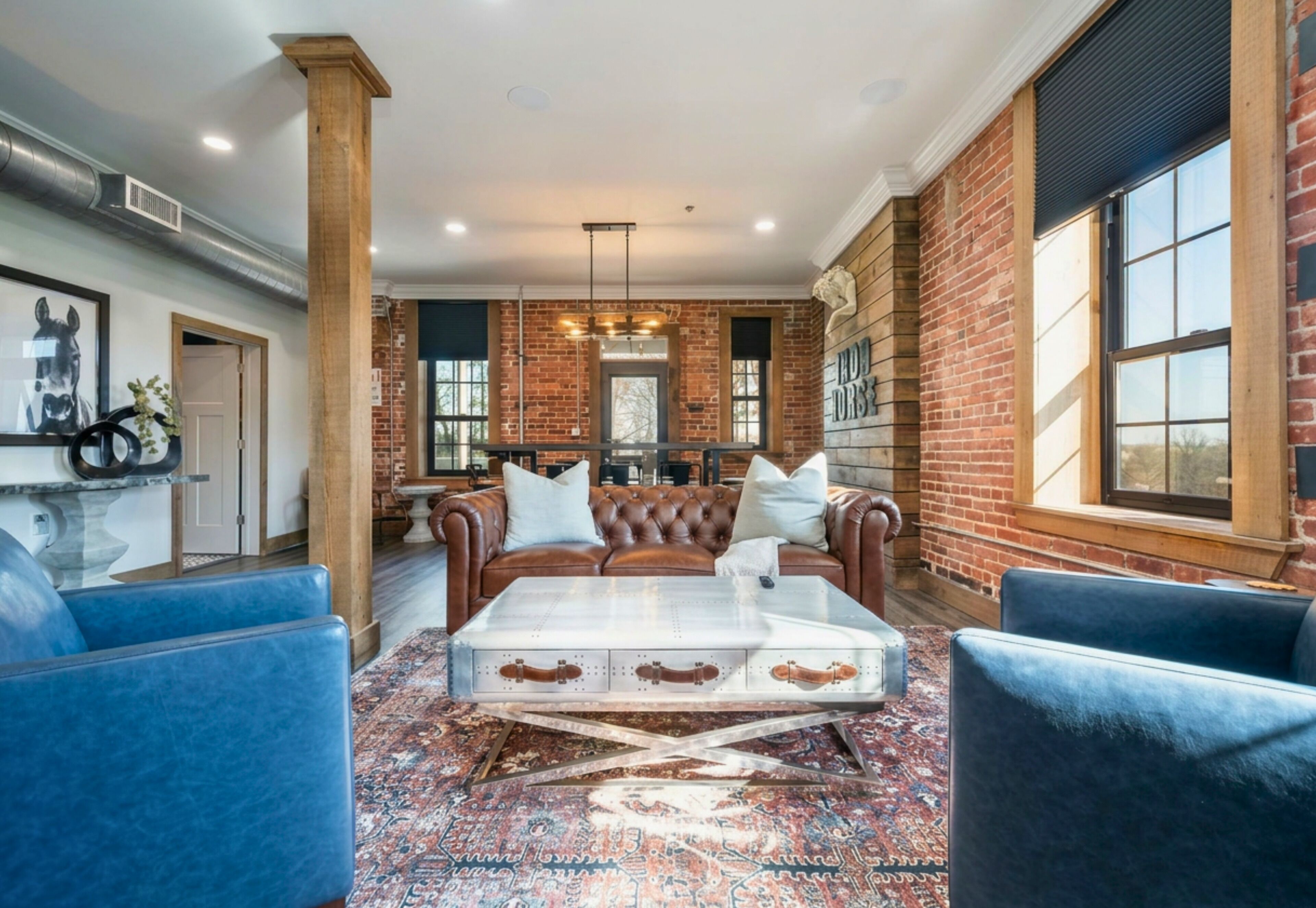 A spacious living room with a large brown leather sofa, a white coffee table, and blue armchairs.