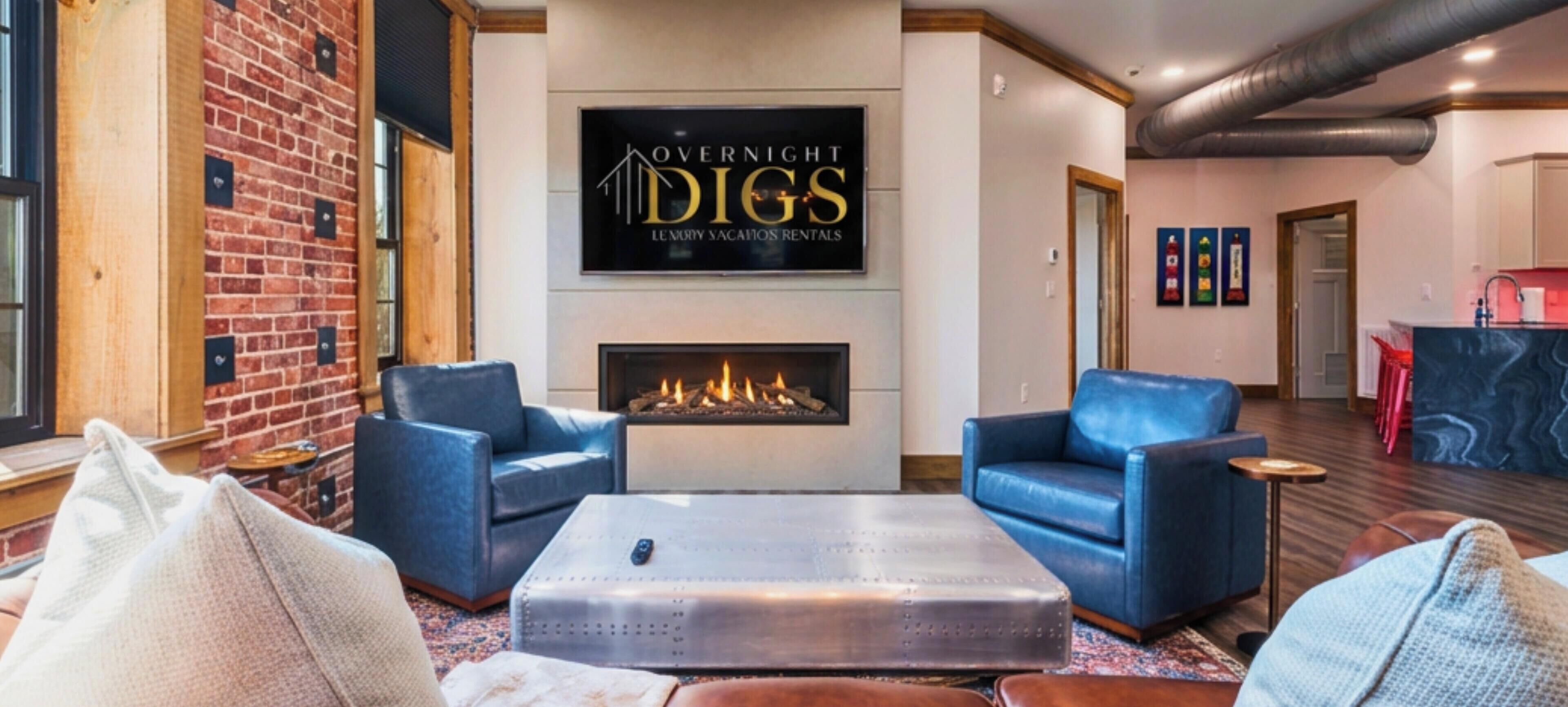 A modern living room with a fireplace, two blue armchairs, a coffee table, and a brick wall.