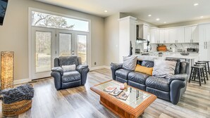 A spacious living room with a large window, a ceiling fan, and a kitchen in the background. - Spacious Hampton Vacation Home Near Beaches! (Hampton)