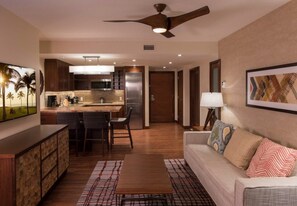 A modern kitchen with a central island, a dining area with chairs, a sofa with patterned cushions, and a ceiling fan.