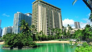 Un grand hôtel doté de nombreux balcons, entouré de palmiers et bordé par une plage.
