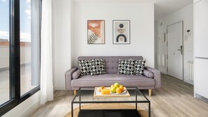 A modern living room with a grey sofa, two patterned cushions, a coffee table with fruit, and two abstract wall art pieces.