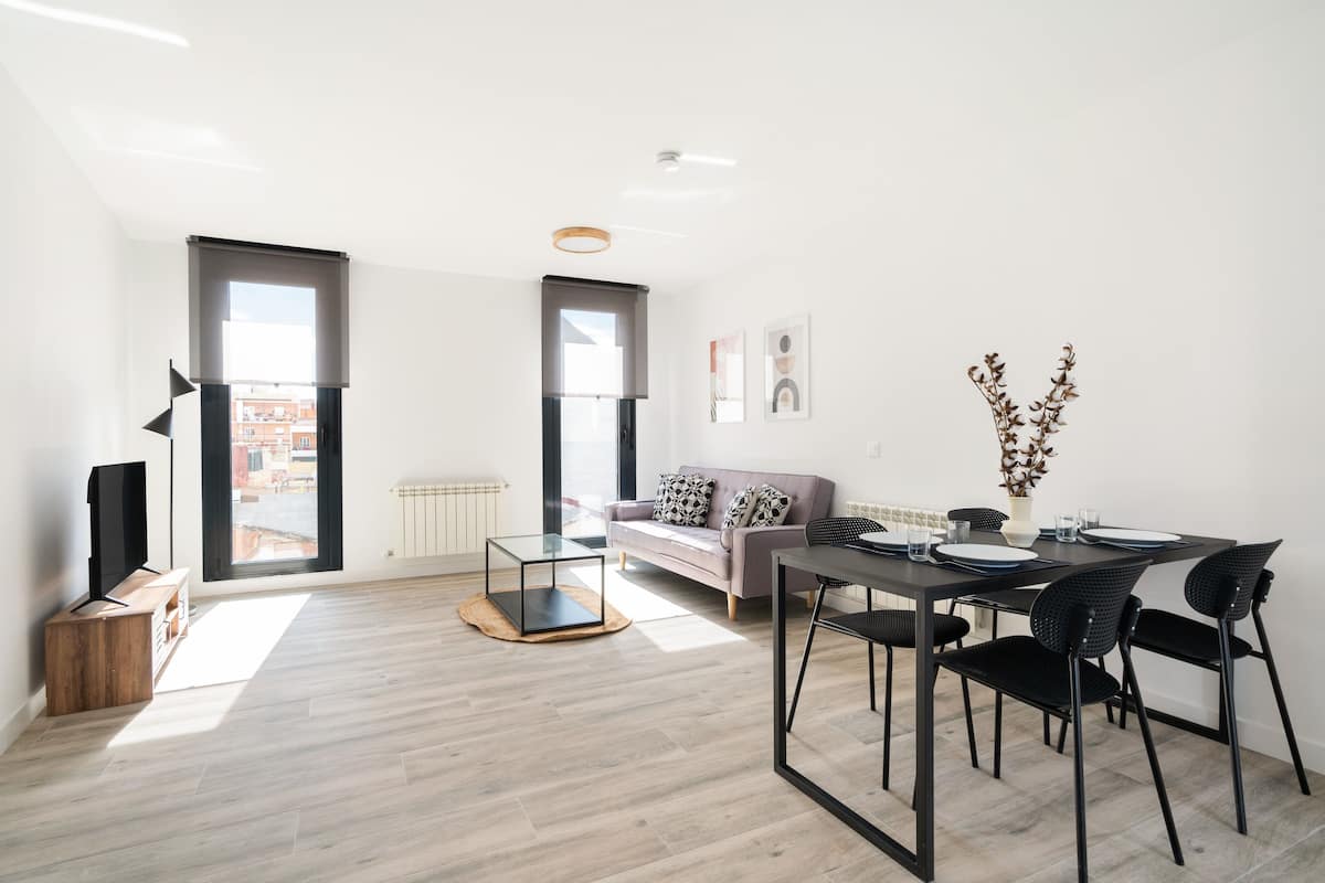 A modern living room with a sofa, a dining table with chairs, and large windows.