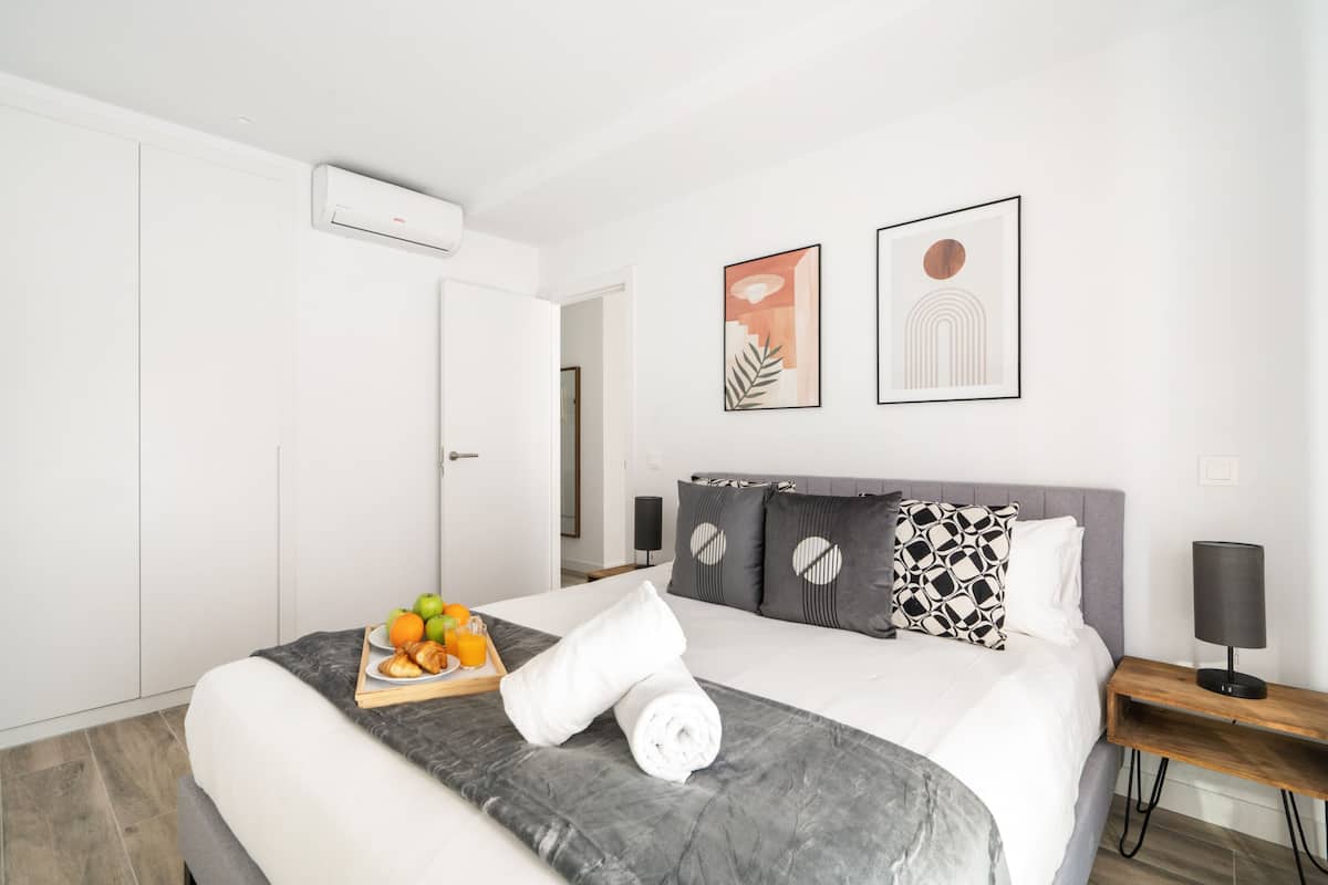 A modern hotel room with a neatly made bed, a tray of fruit, and a bedside table with a lamp.