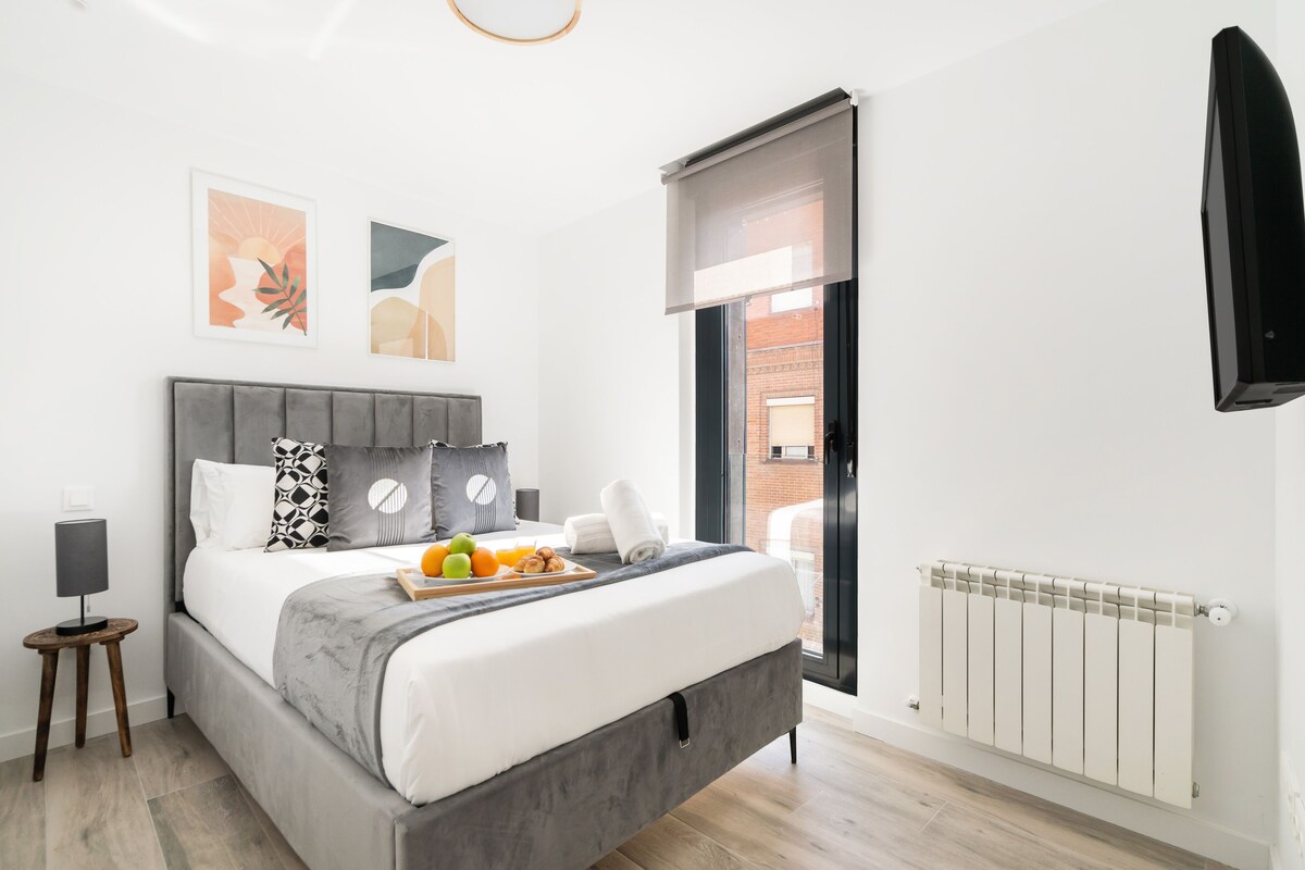 A modern bedroom with a bed, a bedside table, a radiator, and artwork on the wall.