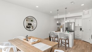 A modern kitchen with white cabinets, a wooden dining table, and a round mirror on the wall.