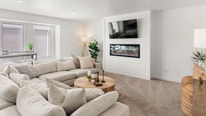 A modern living room with a sectional sofa, a coffee table, and a flat-screen TV mounted on the wall.