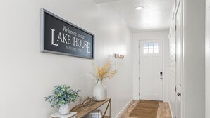 A hallway with a welcome sign, a console table with plants, and a door.
