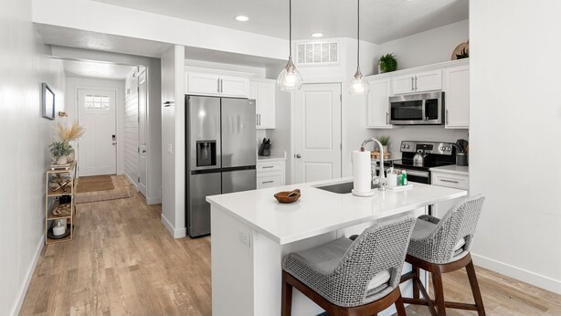 A modern kitchen with white cabinetry, stainless steel appliances, and a central island with bar stools.