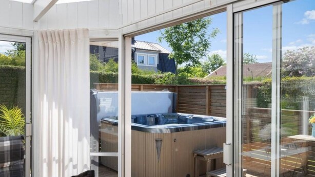 Ein Whirlpool auf einer Holzterrasse mit Glasüren, die zu einem Gartenbereich führen.