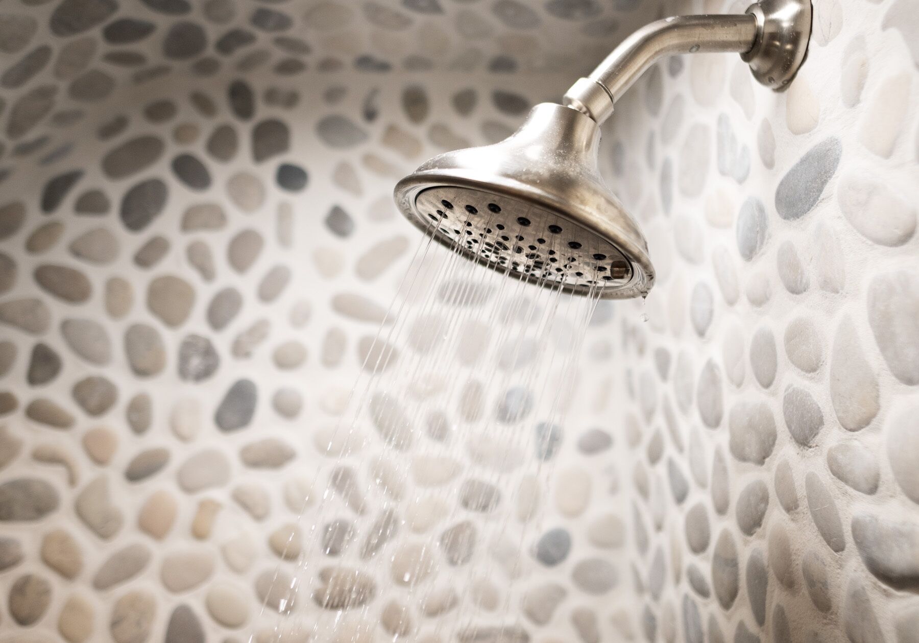 A showerhead with water flowing over a pebble-textured wall.