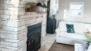 A living room with a stone fireplace, a mounted TV, a white sofa, and a coffee table with a vase of flowers.