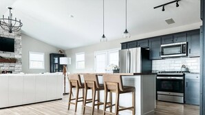 A modern kitchen with a central island, bar stools, a built-in microwave, and a stainless steel oven.