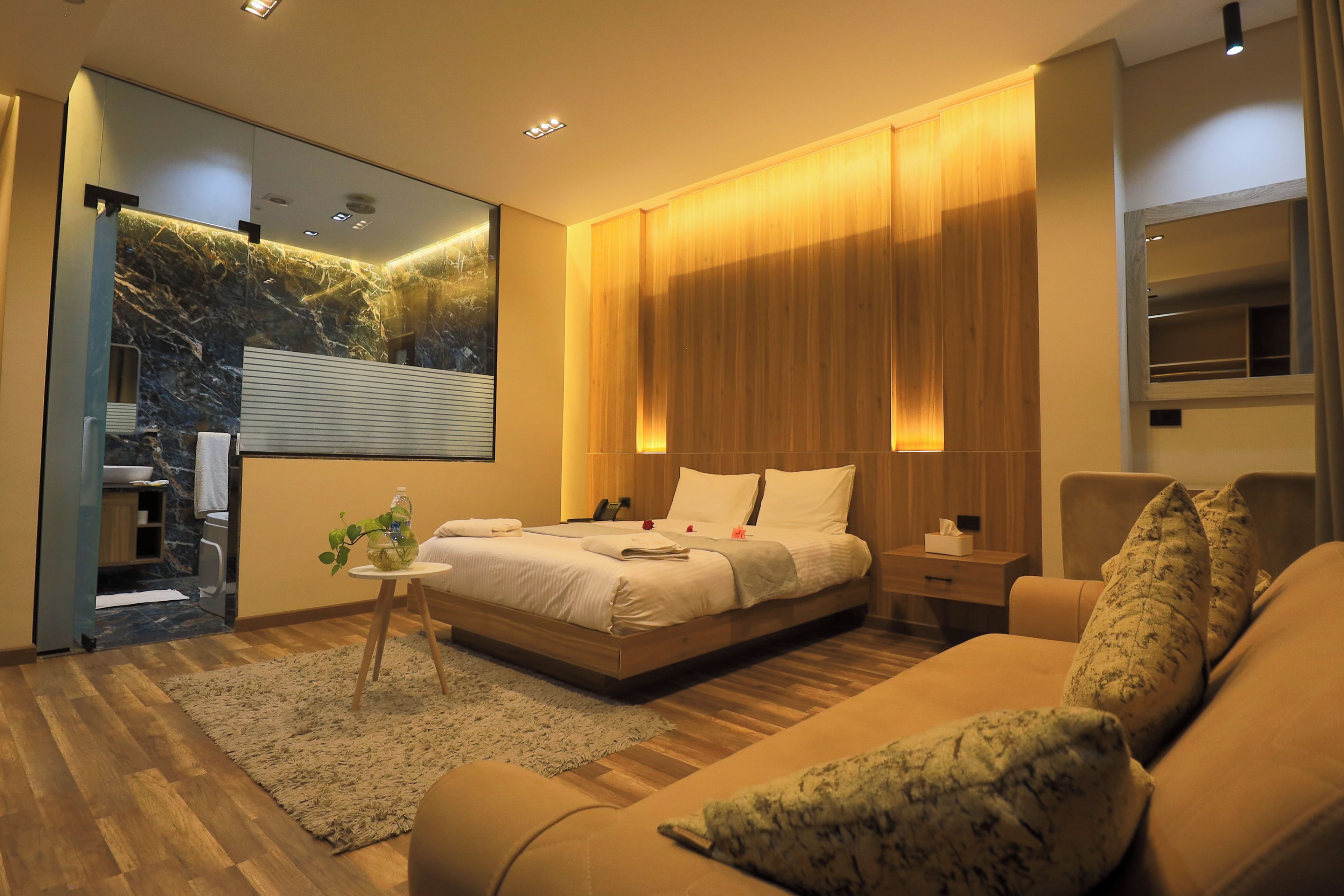 A modern hotel room with a large bed, a sitting area with a sofa, a small table, and a mirror.