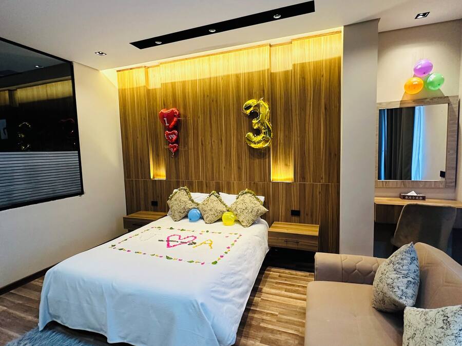 Un dormitorio moderno con cama, sofá, pared decorativa de madera y espejo.