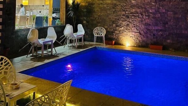 A nighttime view of a swimming pool area with a stone wall and a balcony overlooking the pool. - Farida Palace Hotel Boutique  (Luxor)
