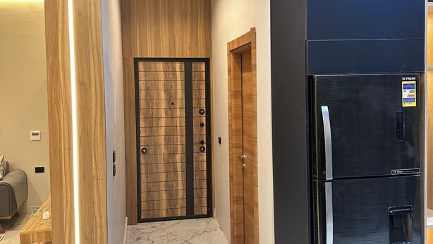 A hallway with a marble floor, wooden doors, and a black refrigerator. - Farida Palace Hotel Boutique  (Luxor)