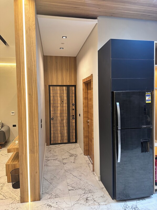A hallway with a marble floor, wooden doors, and a black refrigerator. - Farida Palace Hotel Boutique  (Luxor)