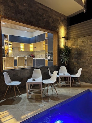 A modern kitchen with dark stone walls and a large mirror reflecting the interior. There are white chairs around a pool area with a blue-lit edge. - Farida Palace Hotel Boutique  (Luxor)
