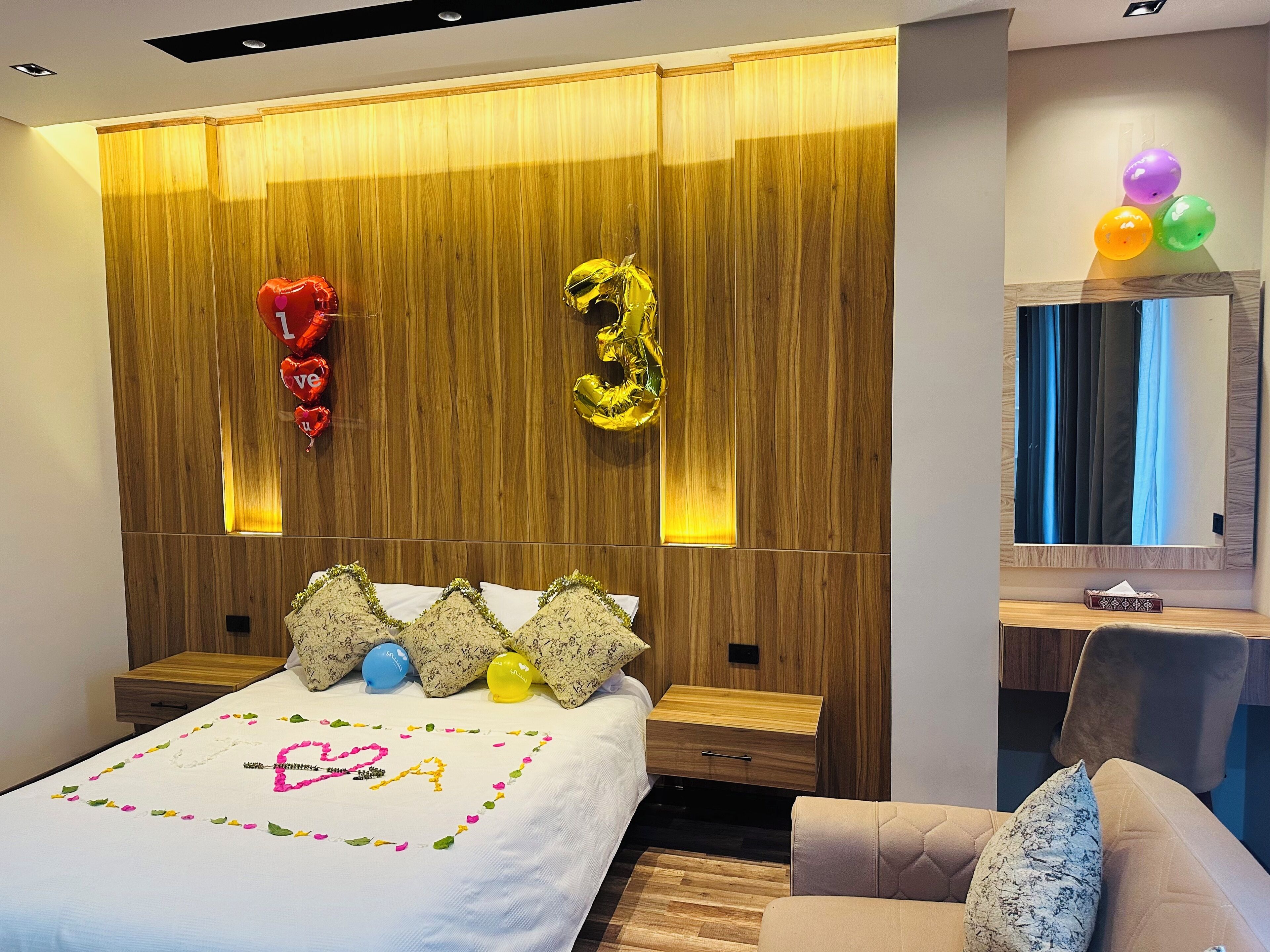 Un dormitorio moderno con cabecera de madera, una cama con decoración en forma de corazón y una mesita de noche con lámpara.