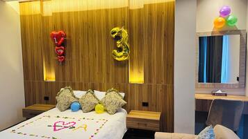 Un dormitorio moderno con cabecera de madera, una cama con decoración en forma de corazón y una mesita de noche con lámpara.