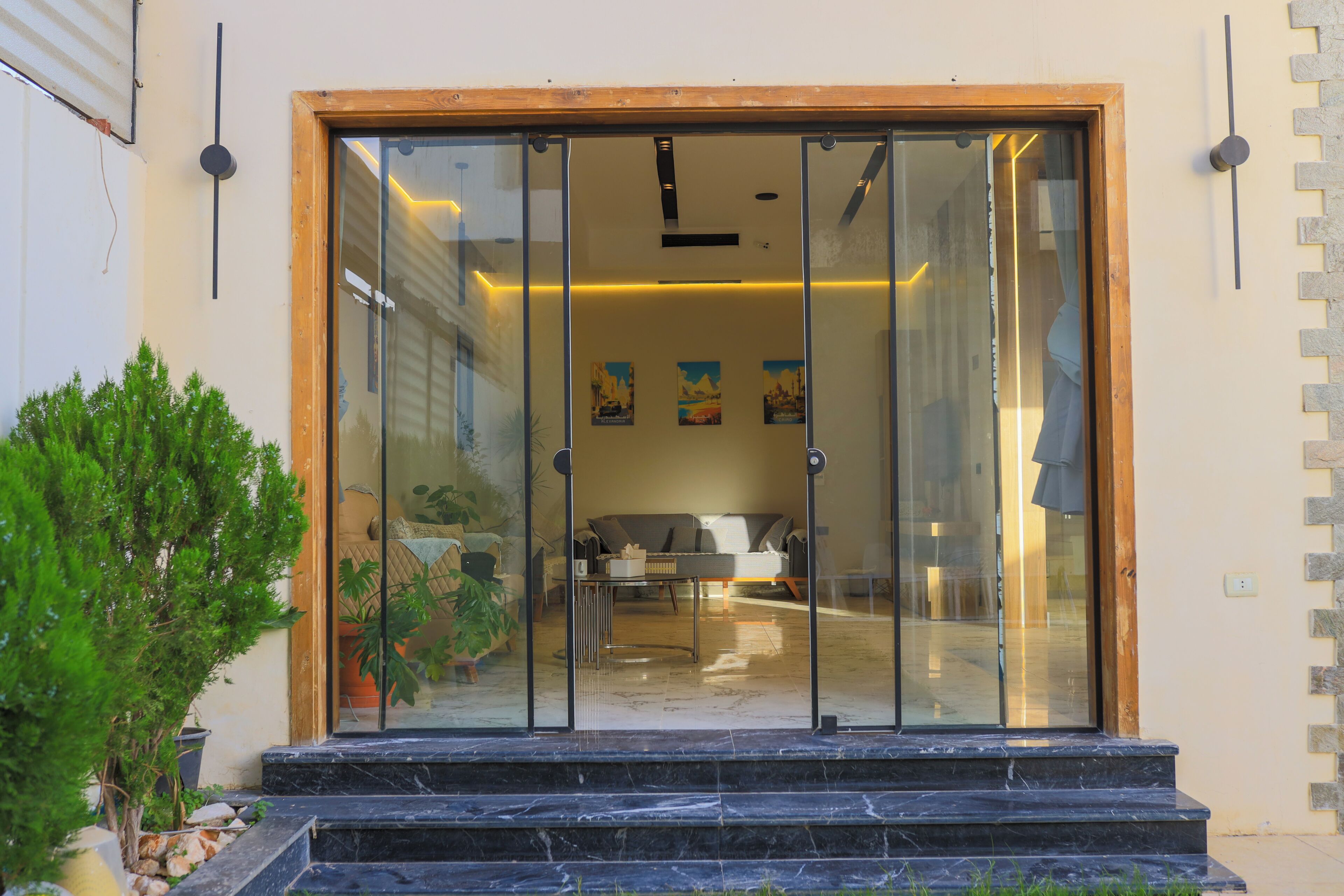 Uma entrada moderna com porta de vidro, um lance de degraus e uma pequena área ajardinada com plantas.