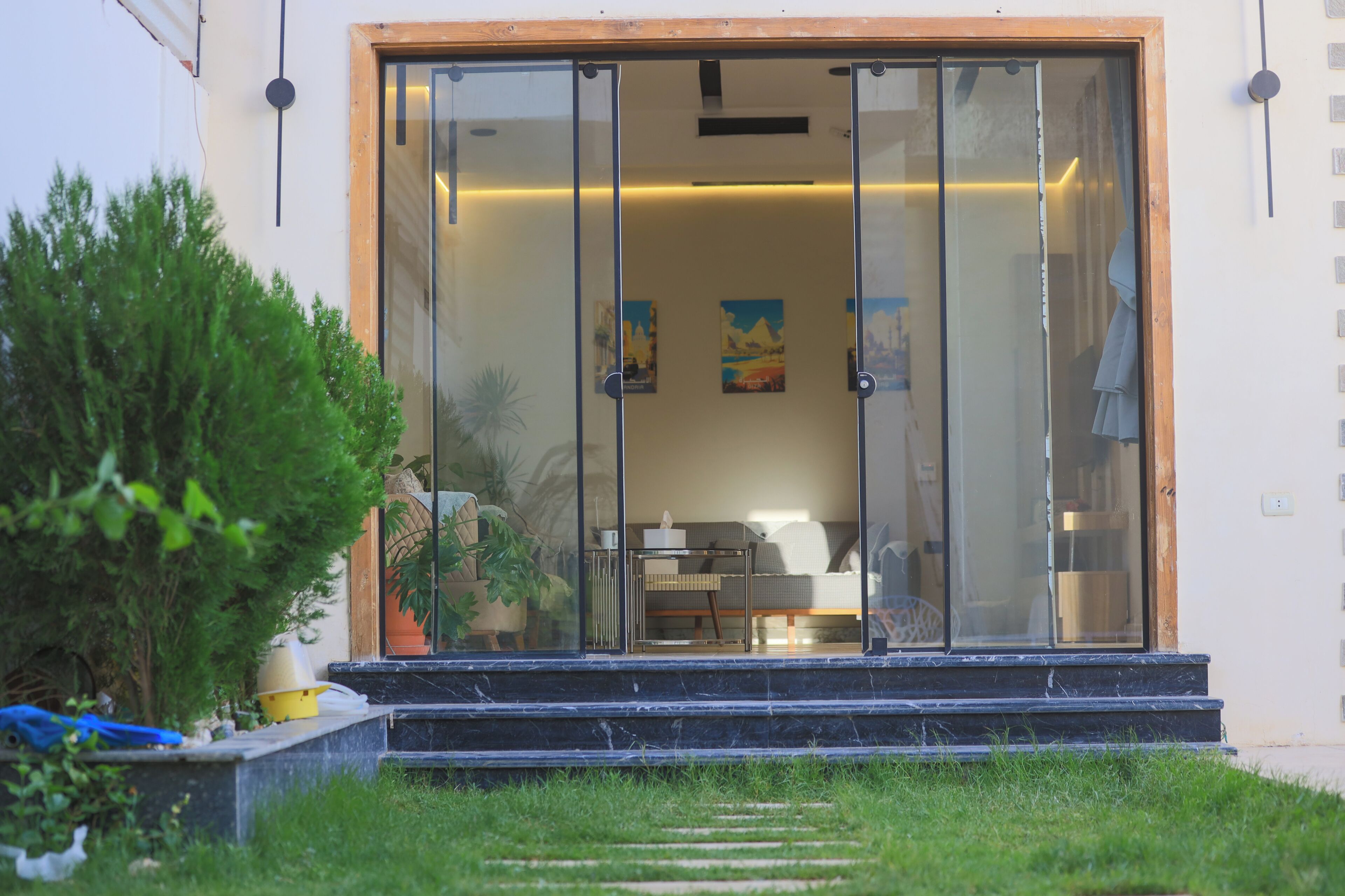 A modern house with a glass door entrance, a small outdoor seating area, and a garden.