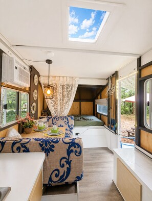 A compact RV interior with a kitchenette, a dining area with a table and chairs, a bed, and a skylight. - Unique Pop-Up Glamping Retreat • Free Parking• Fire Pit • Hammock • Pet Friendly (Hawthorne)