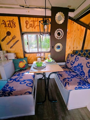 A cozy kitchenette with a window, wooden walls, and a table with a green bowl and a light bulb. - Unique Pop-Up Glamping Retreat • Free Parking• Fire Pit • Hammock • Pet Friendly (Hawthorne)