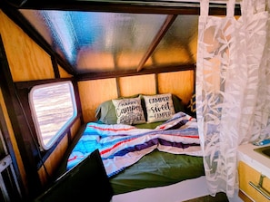 A campervan interior with a bed, two pillows, a laptop, and a window. - Unique Pop-Up Glamping Retreat • Free Parking• Fire Pit • Hammock • Pet Friendly (Hawthorne)