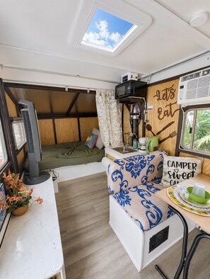 Eine kompakte Küchenzeile für Wohnmobile mit Dachfenster, Mikrowelle, Spüle und Essbereich mit Tisch und Stühlen.