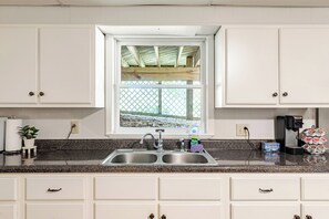 A kitchen with white cabinets, a double sink, a window with a view, and a coffee maker. - Twin Ridge Retreat (Port Royal)