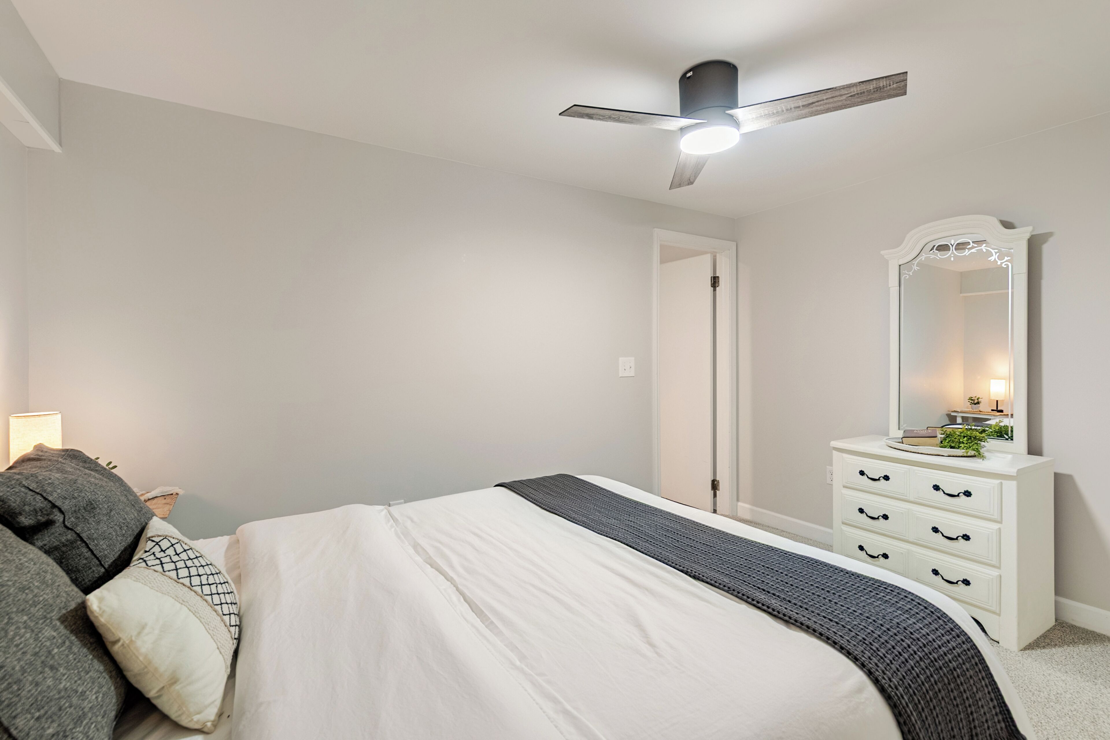 Ein Schlafzimmer mit einem Bett, einer Kommode mit Schubladen, einem Spiegel, einem Deckenventilator und einer Tür.