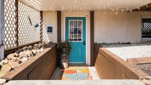 A house entrance with a blue door, a wooden bench, a colorful rug, and a lattice fence. - Twin Ridge Retreat (Port Royal)
