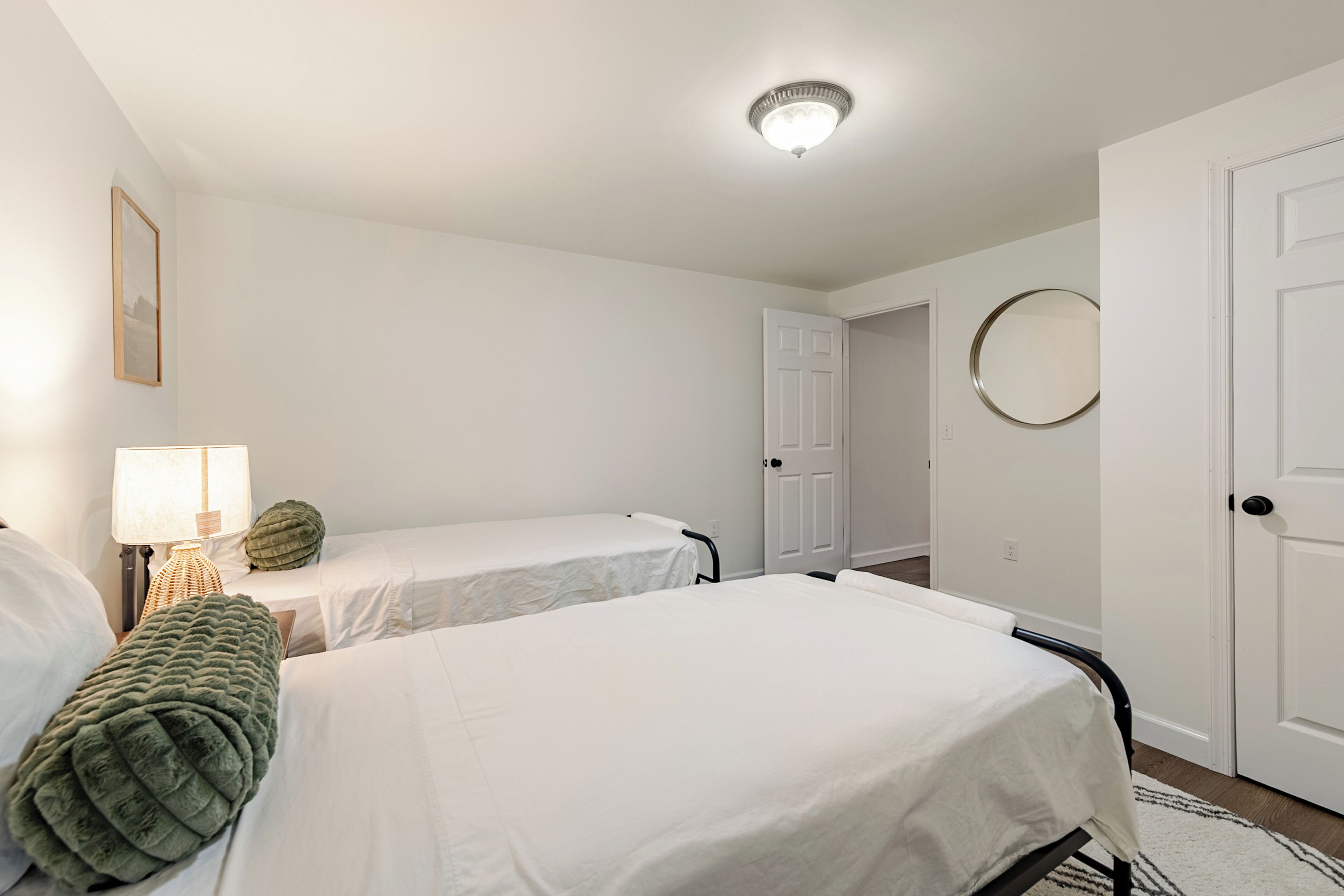 A room with two beds, a bedside lamp, a round mirror, and a door.