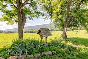 A rural landscape with a wooden birdhouse and a stone structure, surrounded by lush greenery and a field. - Twin Ridge Retreat (Port Royal)