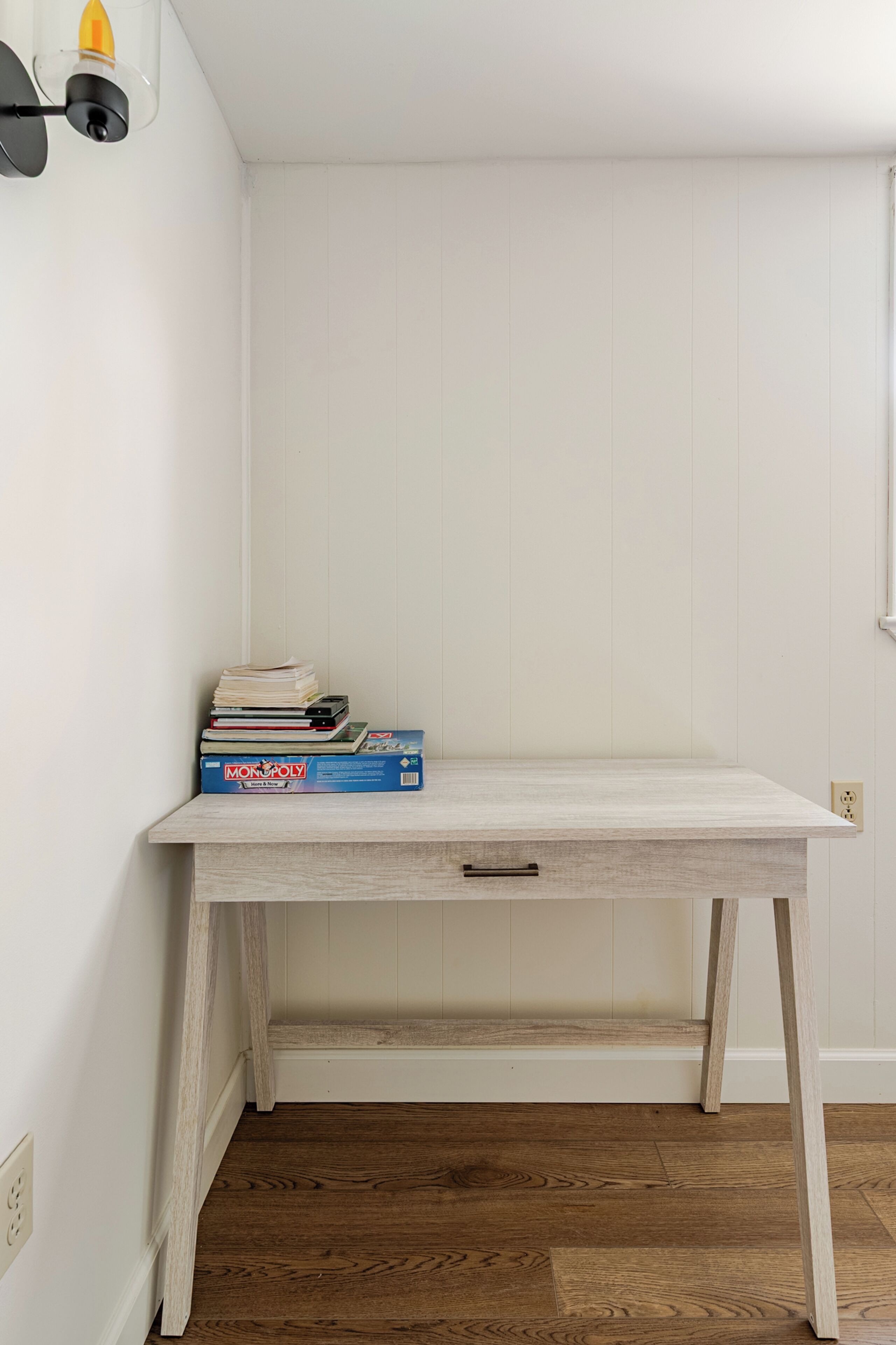 A white wooden desk with a drawer, a Monopoly game box, and some books on it.
