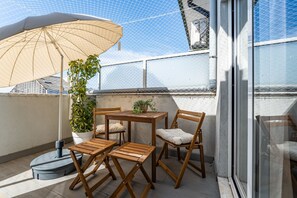 Un balcón con una mesa y sillas de madera, una planta en maceta y un paraguas grande.