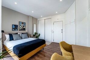 A modern bedroom with a bed, bedside table, lamp, and a chair.