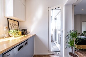 Una cocina con lavavajillas integrado, un lavamanos pequeño y una ventana con vistas a un balcón.