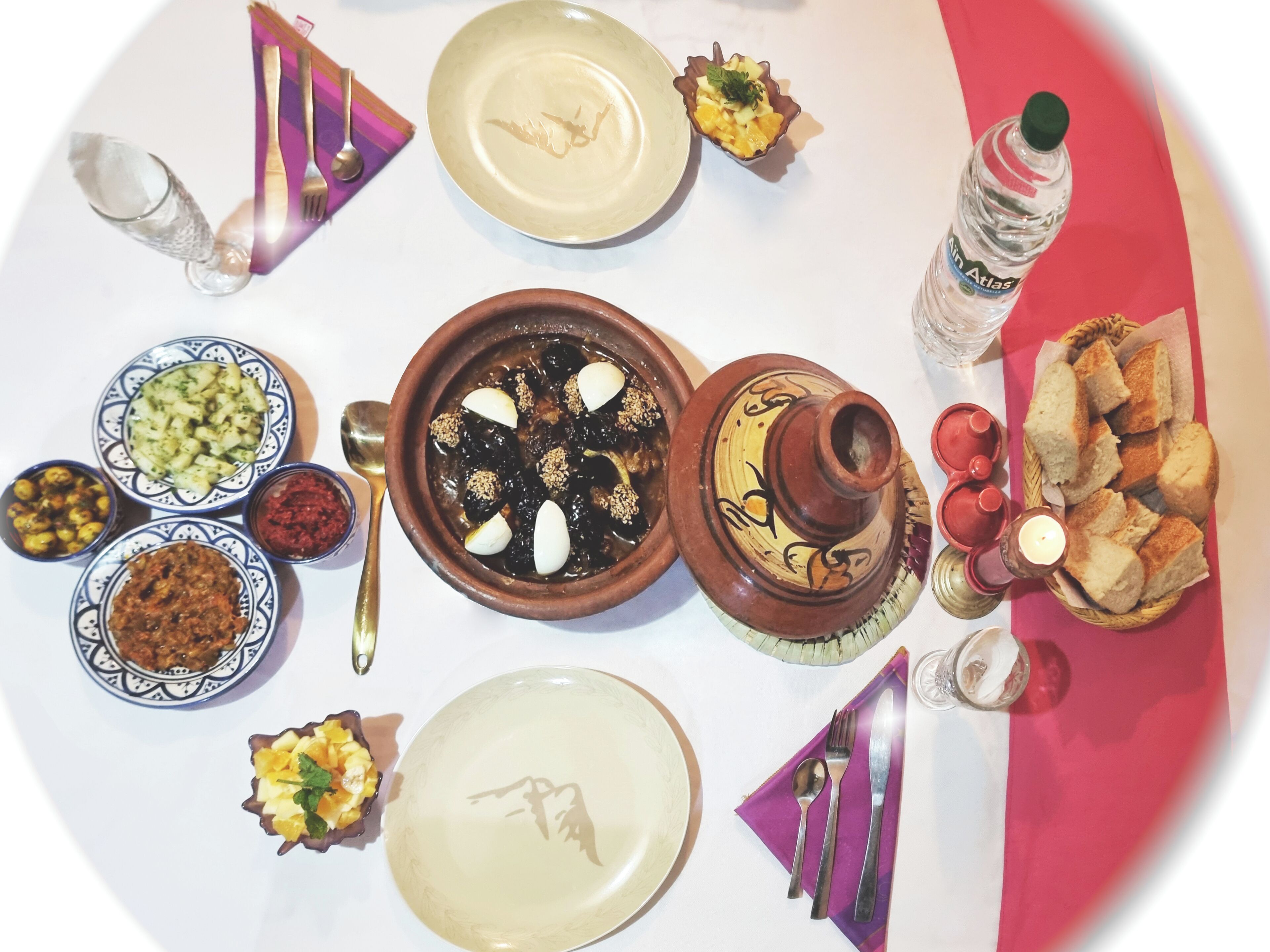 Una mesa dispuesta con diferentes platos, incluyendo un tazón de aceitunas, una rebanada de pan y una botella de agua.