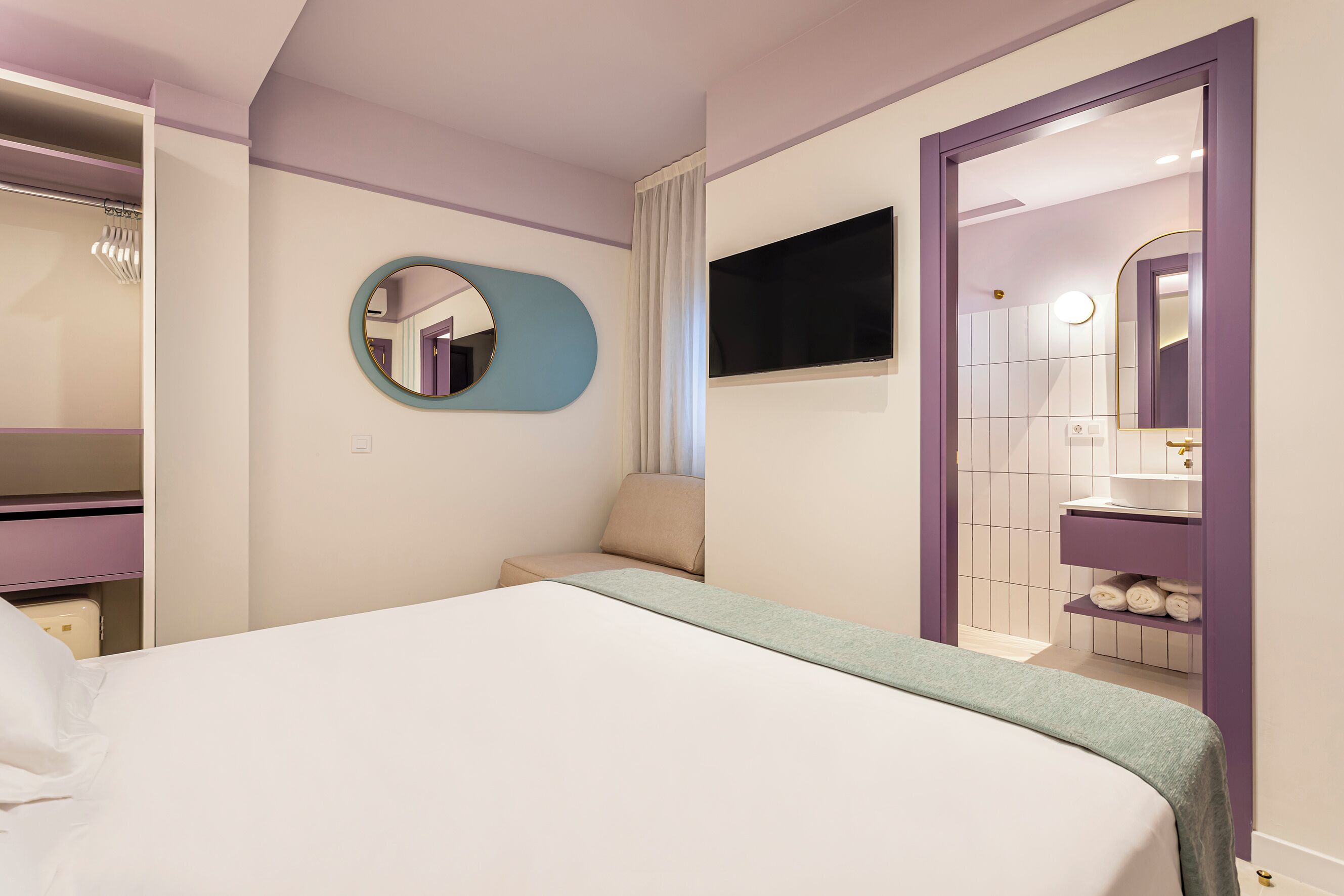 Una camera da letto con un letto, uno specchio, una televisione e un bagno con un lavandino e uno specchio.