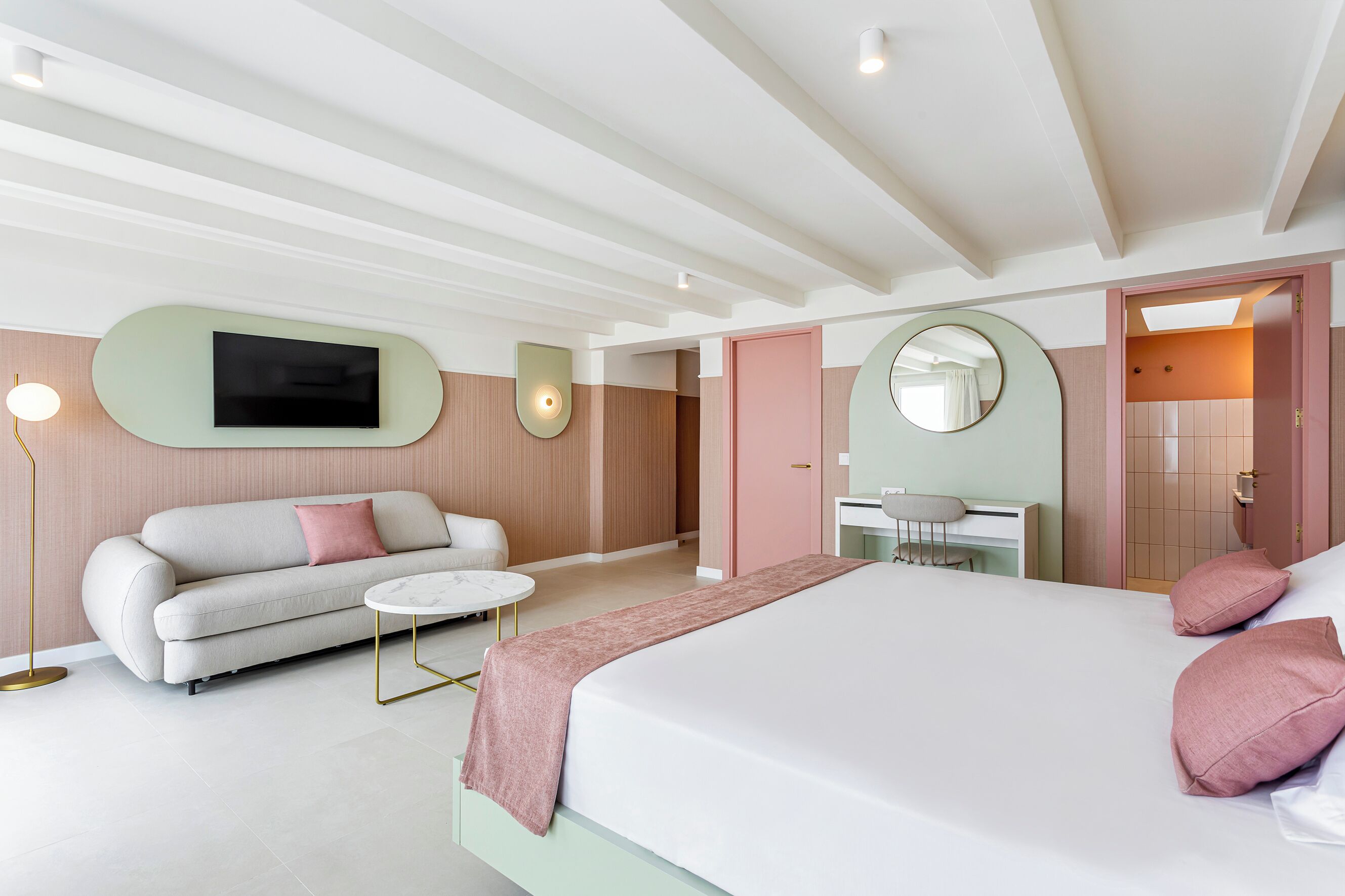 Una habitación de hotel moderna con cama, sofá, televisión, escritorio y espejo.
