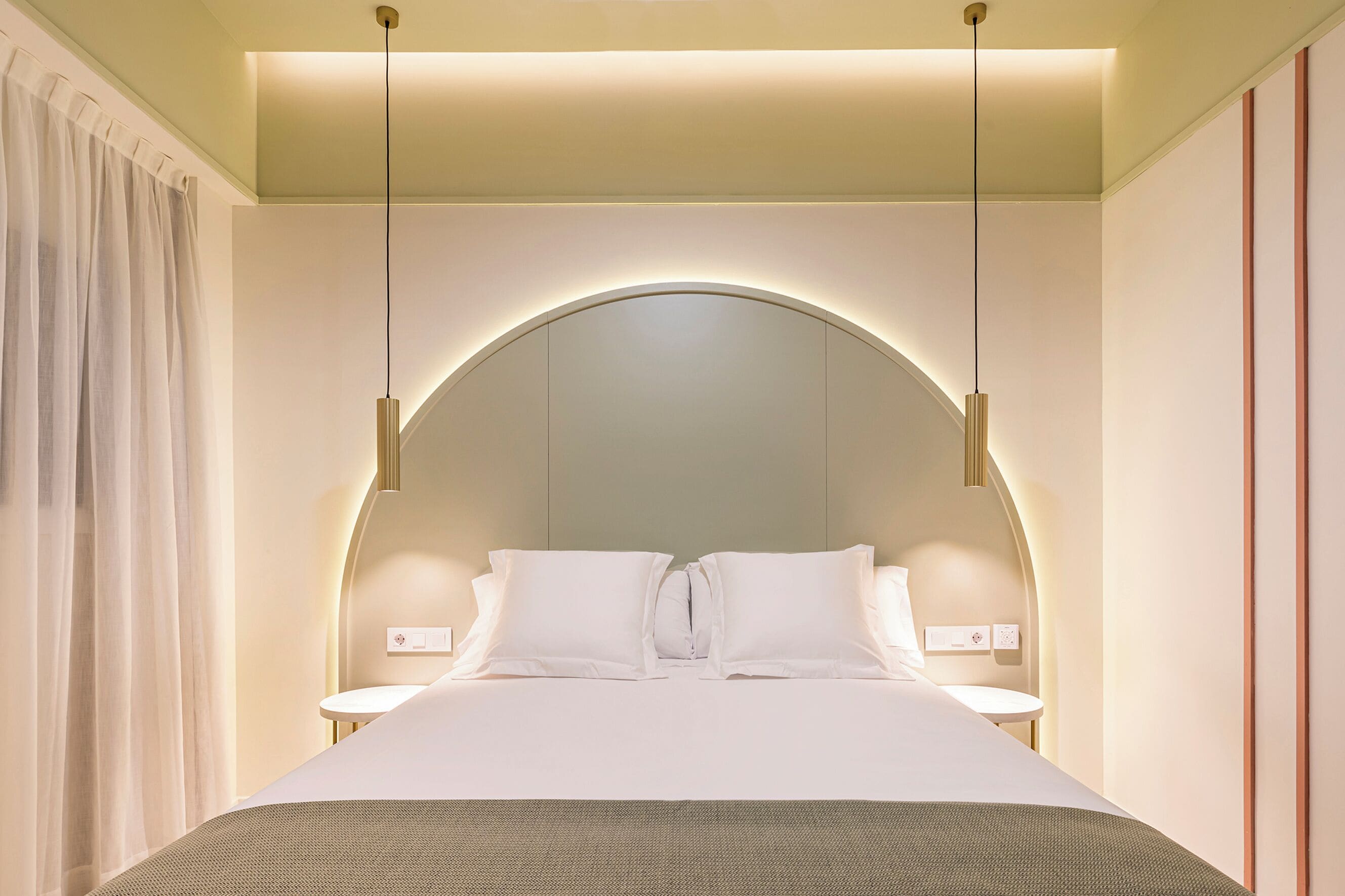Une chambre d’hôtel moderne avec un grand lit, deux tables de chevet et une tête de lit incurvée.