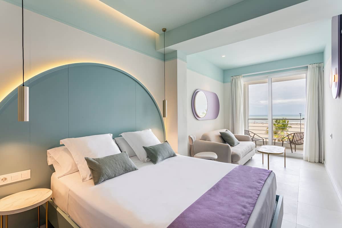 Una habitación de hotel moderna con cama, zona de estar y balcón con vistas.