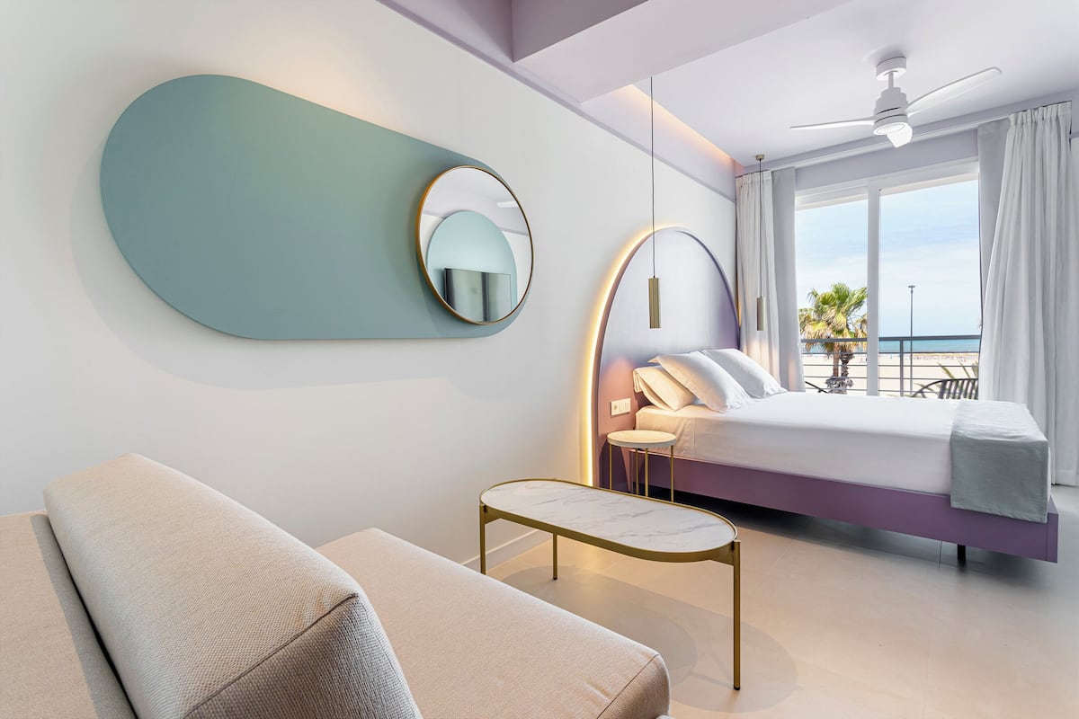 Una habitación de hotel moderna con una cama, un sofá, una mesita y un ventilador de techo, con vista al mar.