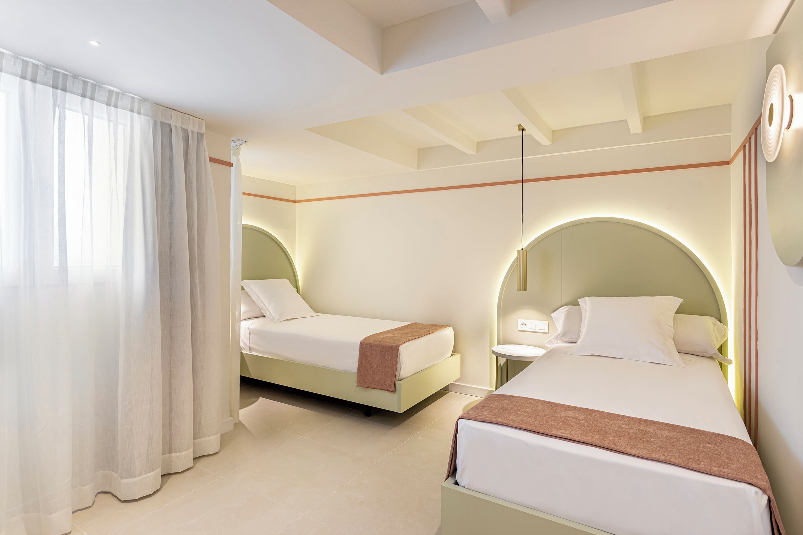 A hotel room with two beds, a large window with curtains, a round mirror, and a modern ceiling design.