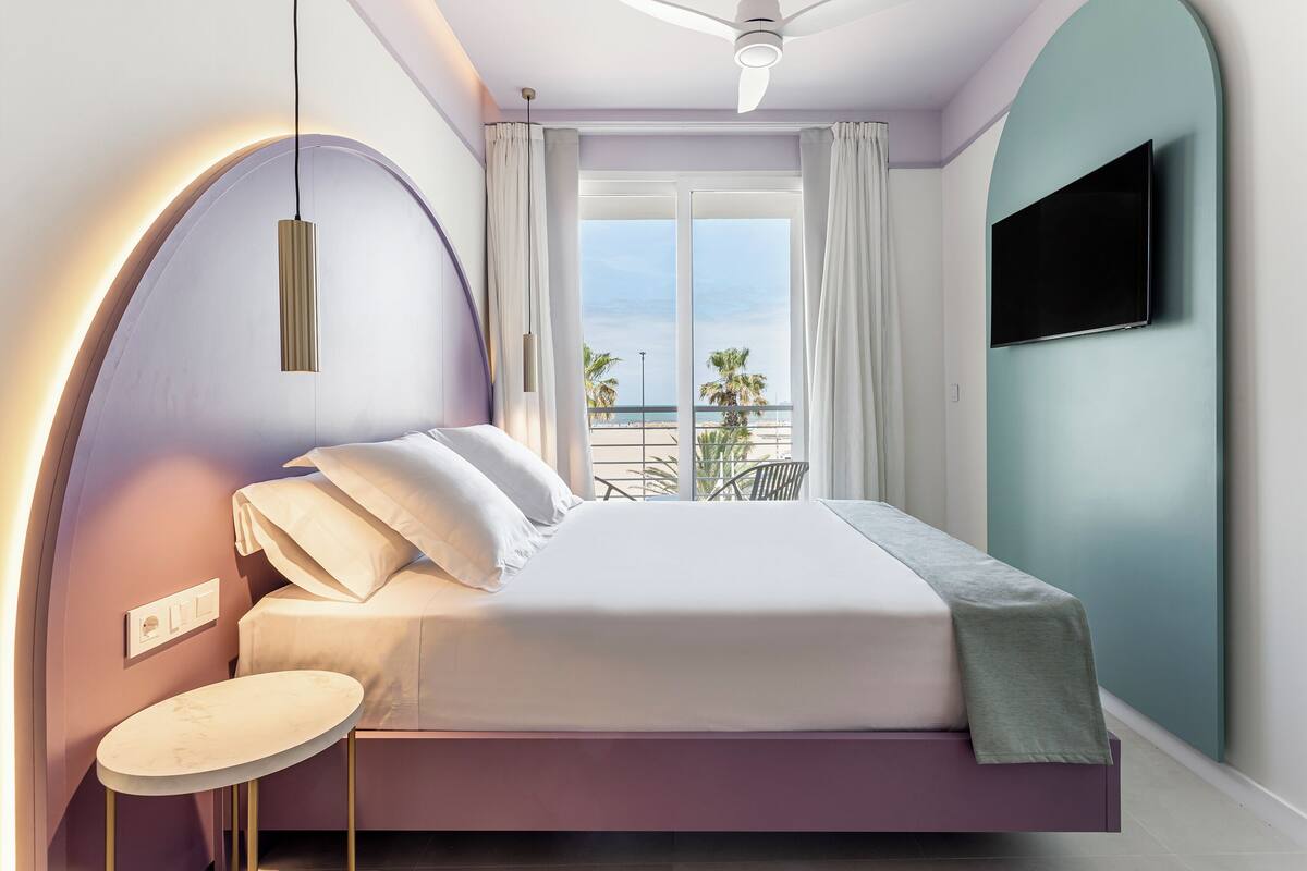 Un dormitorio moderno con cama, una mesa redonda, ventilador de techo y televisor montado en la pared.