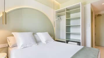 Una cama bien hecha con sábanas blancas, un armario empotrado con puertas abiertas y una mesita de noche con una lámpara.