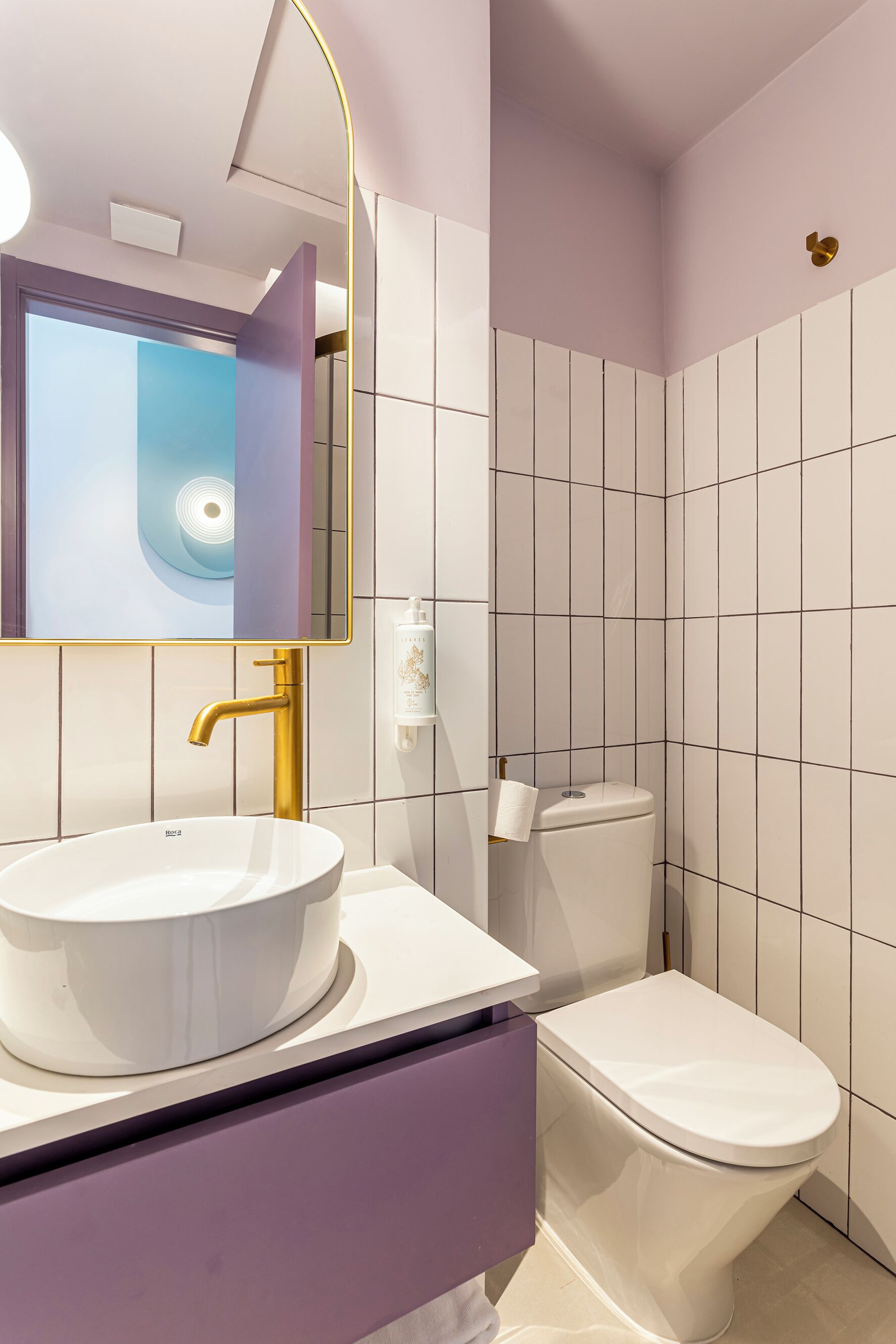 Et moderne badeværelse med en hvid vask, guldfarvet hanefaucet og et toilet.